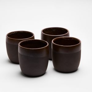 Vier handgefertigte schwarze Steinzeugbecher, halb glasiert und im Set arrangiert.